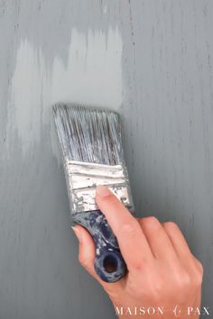 a hand holding a paint brush over a gray wall