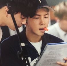 two young men are looking at a book and one is holding an orange object in his mouth