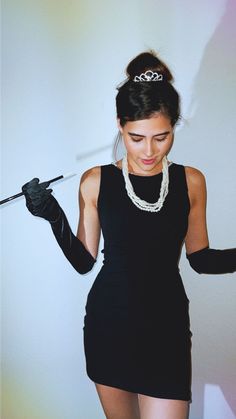 a woman in a short black dress holding a wand and wearing gloves with pearls on her head