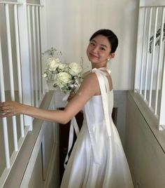 a woman in a white dress holding a bouquet of flowers on her hand and smiling at the camera