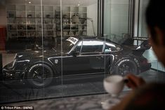 the reflection of a black sports car in a glass window at a coffee shop with a person holding a cup