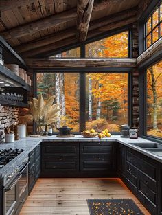 a kitchen with wood flooring and black cabinets in front of a large window that looks out onto the woods