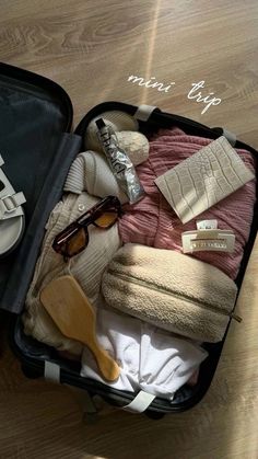 an open suitcase filled with clothing and shoes on top of a wooden floor next to a pair of sunglasses