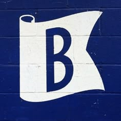 a blue and white sign with the letter b painted on it's side in front of a brick wall