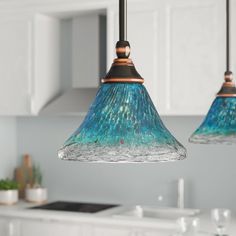 two blue glass lights hanging from a kitchen ceiling over a sink and counter top with white cabinets