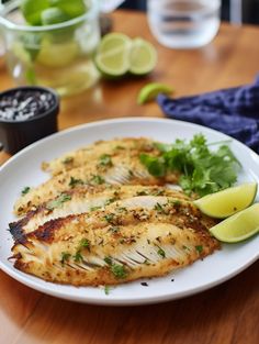 two fish fillets on a white plate with lime wedges next to the side