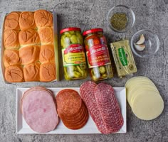 an assortment of meats, cheese and bread on a plate next to some pickles