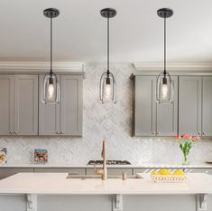 three lights hanging over a kitchen island in a home with gray cabinets and marble counter tops