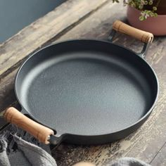 an empty frying pan sitting on top of a wooden table next to a potted plant