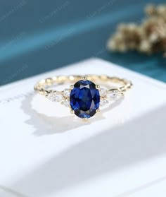 an oval blue sapphire and diamond ring on top of a white card with flowers in the background