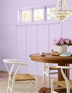 a dining room with purple walls and white chairs around a wooden table that has flowers on it