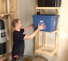 a man holding a blue container in his hand and standing next to a shelf with two black bins on it