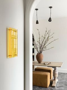 a vase with flowers is sitting on a table next to a yellow light fixture and two stools