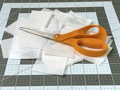 an orange pair of scissors sitting on top of some white pieces of paper next to each other