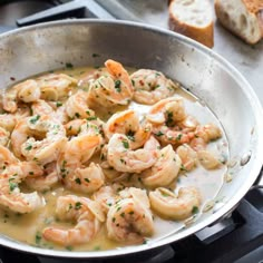 a pan filled with shrimp on top of a stove next to slices of toasted bread