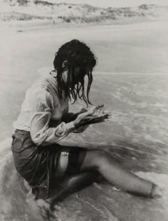 black and white photograph of a woman sitting on the beach with her legs in the water