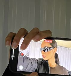 a person holding up a cell phone to take a selfie with her hand and wearing sunglasses