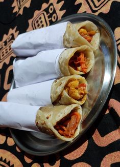 three burritos sitting on top of a metal plate next to a napkin holder