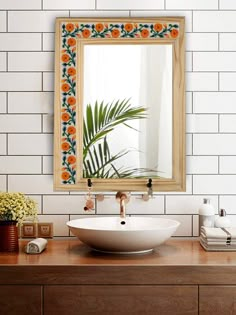 a bathroom sink sitting under a mirror on top of a wooden counter next to a vase with flowers