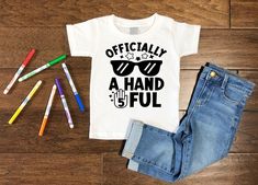 a t - shirt that says officially a hand full with sunglasses and pencils next to it