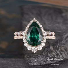 a green and white diamond ring on top of a black stone slab with pearls around it