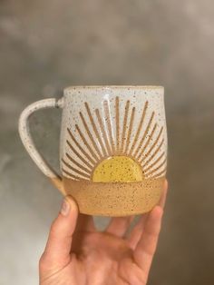 a hand holding up a coffee cup with the sun painted on it