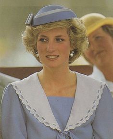 a woman wearing a blue and white dress with a hat on her head, standing next to an older man