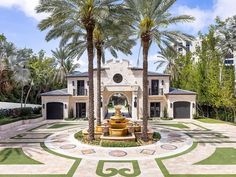 a large house with palm trees and a fountain in the middle of the front yard