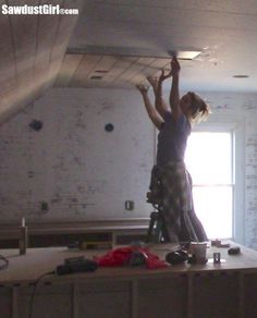 a woman standing on top of a kitchen counter reaching up to the ceiling with her hands