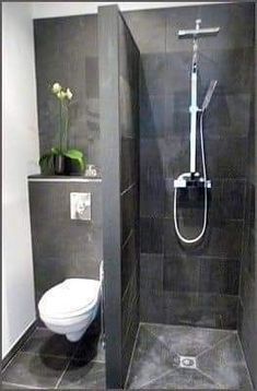 a bathroom with a toilet, shower head and standup shower in grey tile walls