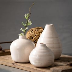 three white vases sitting on top of a wooden tray next to a wicker basket