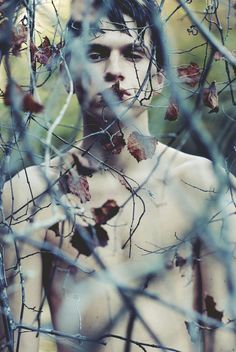 a shirtless man standing in the woods with leaves all over his body and chest