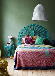 a bedroom with green walls and wooden flooring has a peacock headboard on the bed