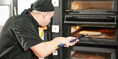 a man in black shirt and bandana looking at an oven with pizzas inside