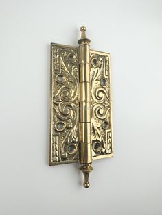 an antique brass door hinge with decorative designs on the front and back sides, mounted on a white wall