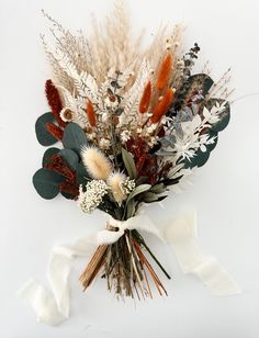 an arrangement of dried flowers and foliage on a white background with ribbon tied around it