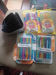 there are many different colored pens in the box on the table next to each other