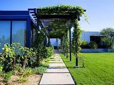 the walkway is lined with green plants and flowers in front of a blue building that has glass windows