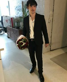 a man in a suit and tie holding a bouquet of flowers while standing next to a door