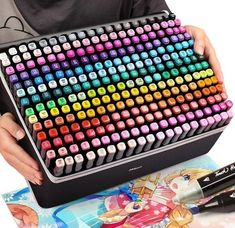 a person holding a large multicolored keyboard in front of a book and some pens