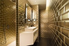 a bathroom with gold tiles on the wall and sink in the middle, along with a mirror