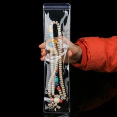 a person holding a long beaded necklace in a clear plastic case on a black background