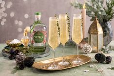 three champagne flutes are sitting on a gold platter with pine cones and greenery