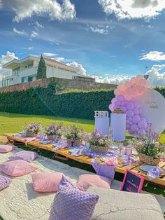 a table set up for a party with purple and pink decorations on it, in the middle of a grassy area