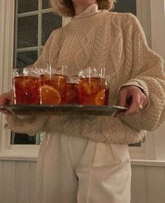 a woman holding a tray full of glasses filled with orange slices and water in front of her face