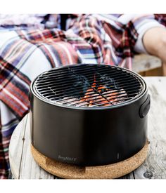 a person laying on a wooden table next to a bbq with flames in it