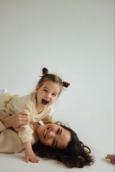 a woman holding a baby in her arms and smiling at the camera while laying on the floor