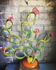 an orange vase with green and pink flowers in it sitting on a wooden stand next to a brick wall