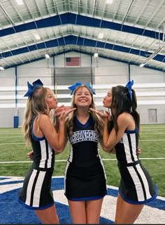 three girls in cheerleader outfits standing on a football field with one girl making a funny face