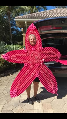 a woman standing next to a car holding a large pink object in front of her